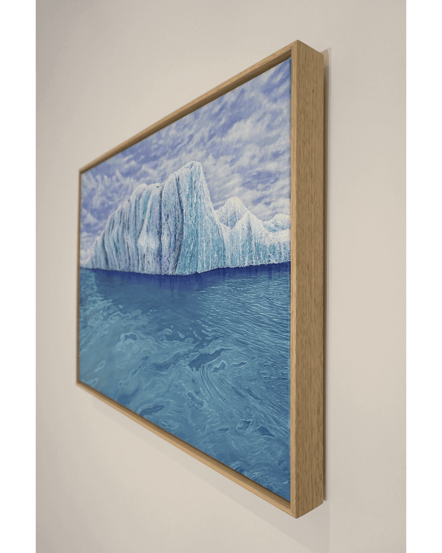 Original art, titled Ammonite, painted in oil on canvas, by Australian artist, Hayley Byron. The painting is a depiction of an iceberg, with clouds in the background, and water in the foreground. This image features the artwork on a wall in a custom-made Tasmanian oak frame.