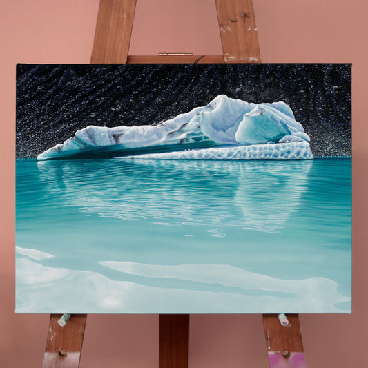 Original art, titled Chrysocolla, painted in oil on canvas, by Australian artist, Hayley Byron. The painting is a depiction of an iceberg, with glacial till in the background, and water in the foreground. This image features the artwork on an easel in an art studio.