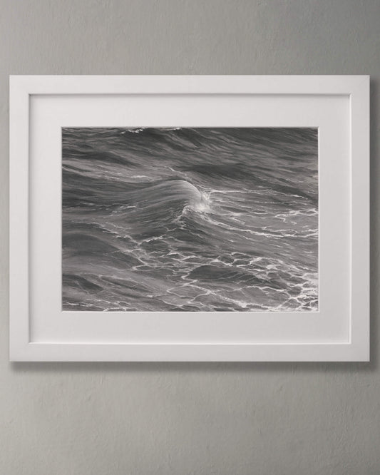 Original art, titled Rise, by Australian artist, Hayley Byron, created with graphite, charcoal, watercolour pencil, and gouache on fine art paper. This drawing is a depiction of the ocean at Tamarama, Sydney, from the viewpoint of the headland cliffs. This image features the artwork in-situ, on a wall in a frame.