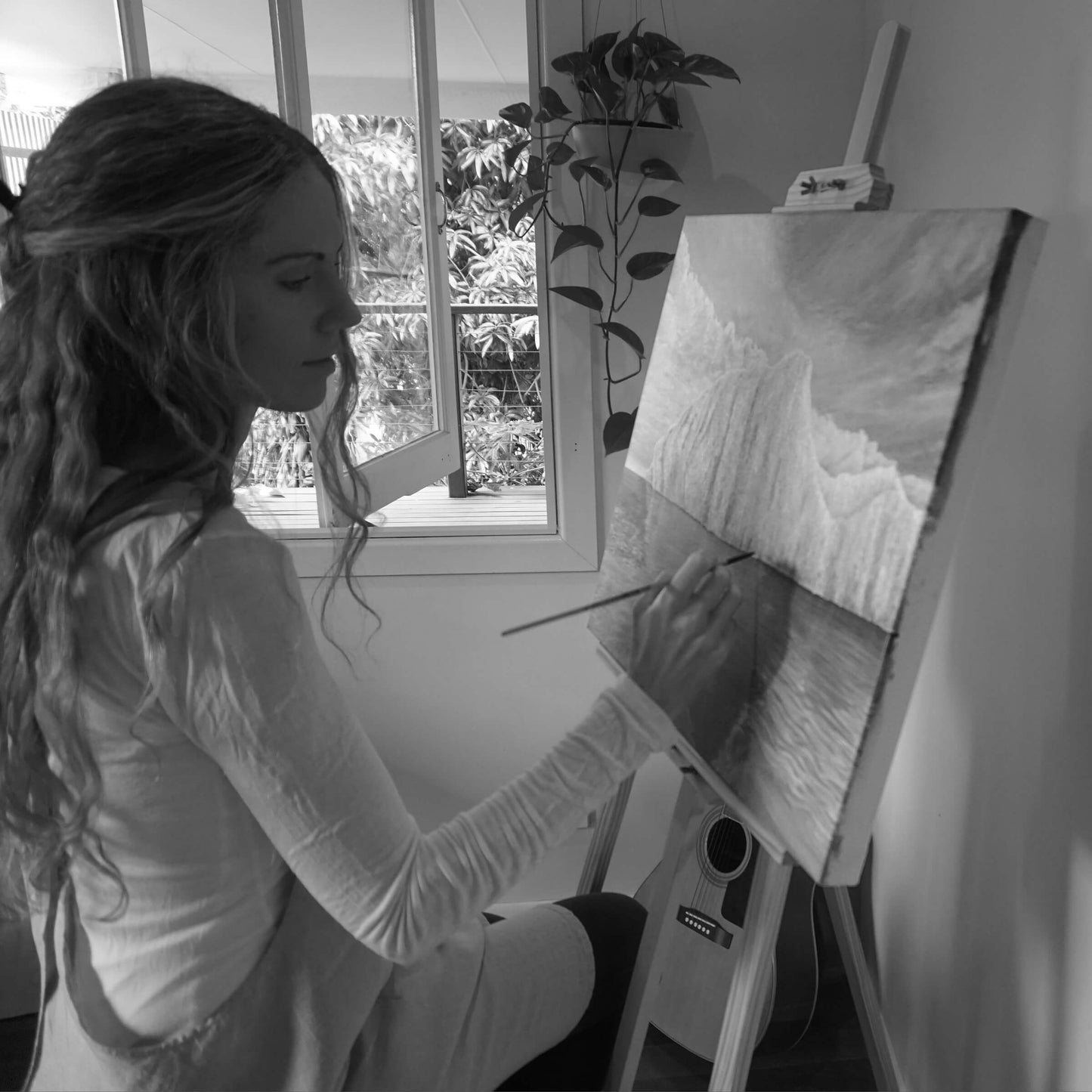 Australian artist, Hayley Byron, painting a depiction of an iceberg in oil on linen. This image features the artist painting on the canvas with a paintbrush, while sitting at an easel. The title of this work is Ametrine.