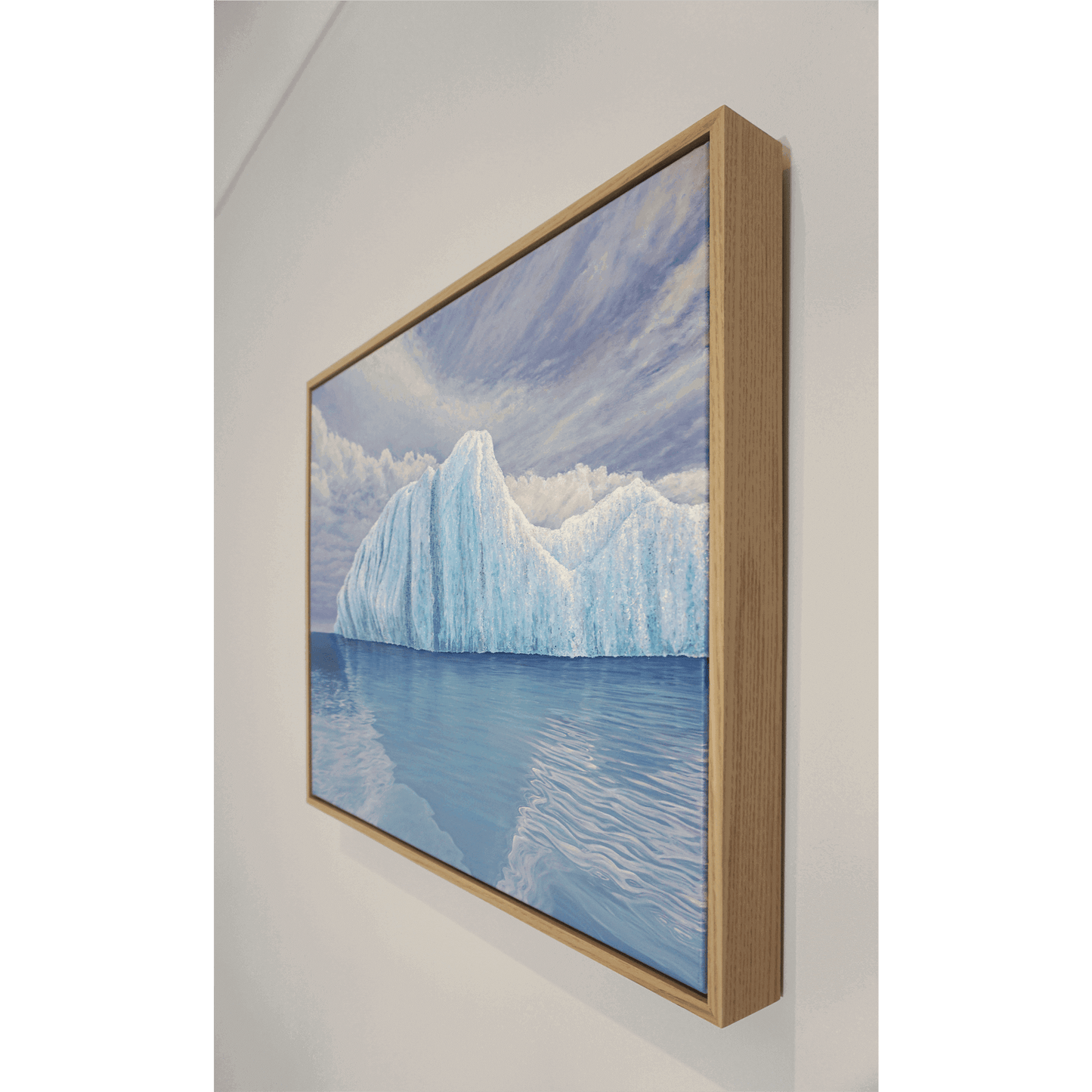 Original art, titled Ametrine, painted in oil on linen, by Australian artist, Hayley Byron. The painting is a depiction of an iceberg, with clouds in the background, and water in the foreground. This image features the artwork on a wall in a custom-made Tasmanian oak frame.