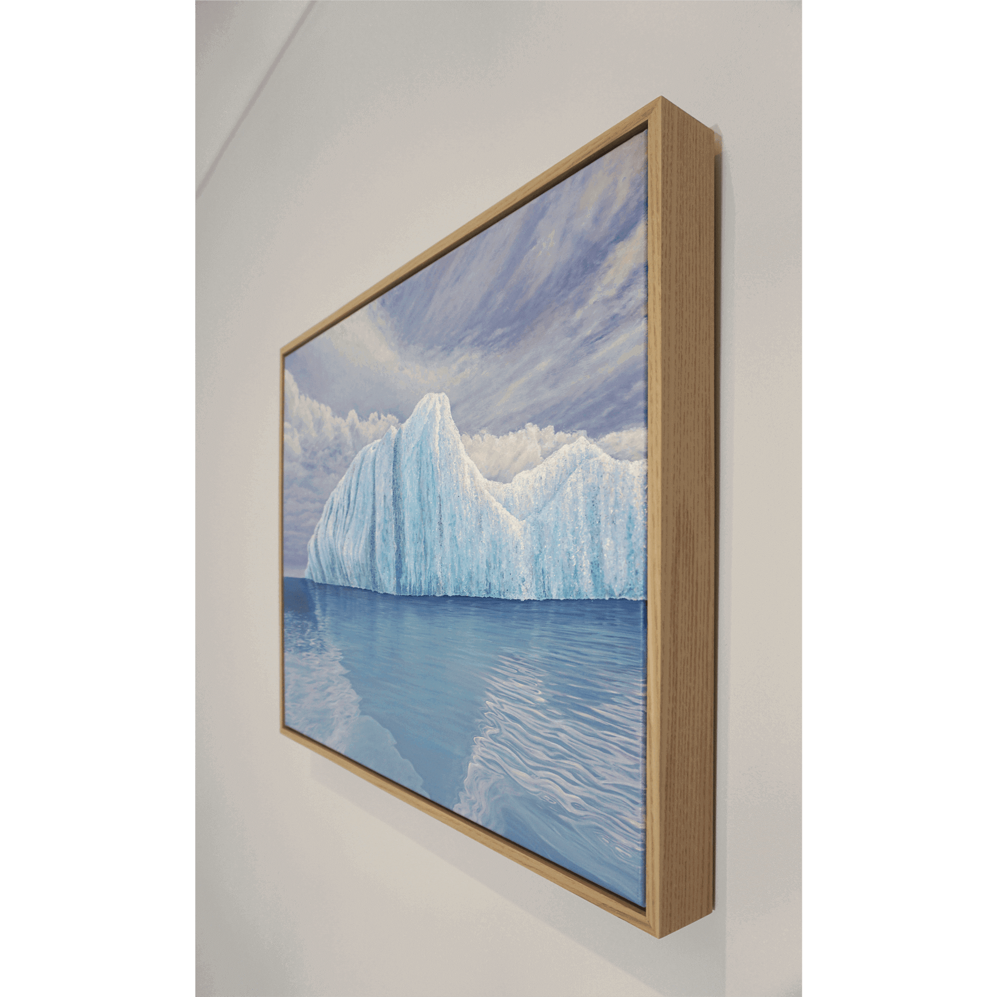 Original art, titled Ametrine, painted in oil on linen, by Australian artist, Hayley Byron. The painting is a depiction of an iceberg, with clouds in the background, and water in the foreground. This image features the artwork on a wall in a custom-made Tasmanian oak frame.