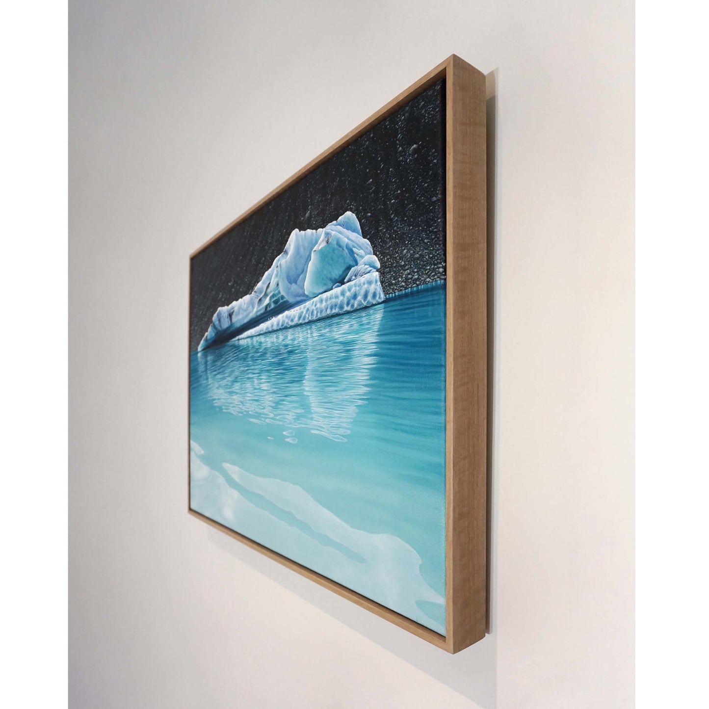 Original art, titled Chrysocolla, painted in oil on canvas, by Australian artist, Hayley Byron. The painting is a depiction of an iceberg, with glacial till in the background, and water in the foreground. This image features the artwork on a wall in a custom-made Tasmanian oak frame.