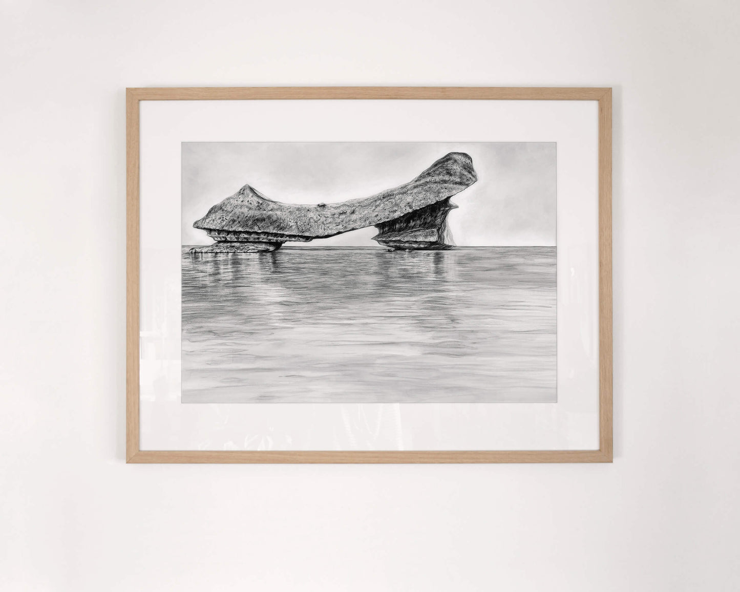Original art, titled Grit, hand-drawn with graphite on fine art paper, by Australian artist, Hayley Byron. The drawing is a depiction of an iceberg, with water in the foreground. This image features the artwork in-situ, on a wall in a custom-made frame.
