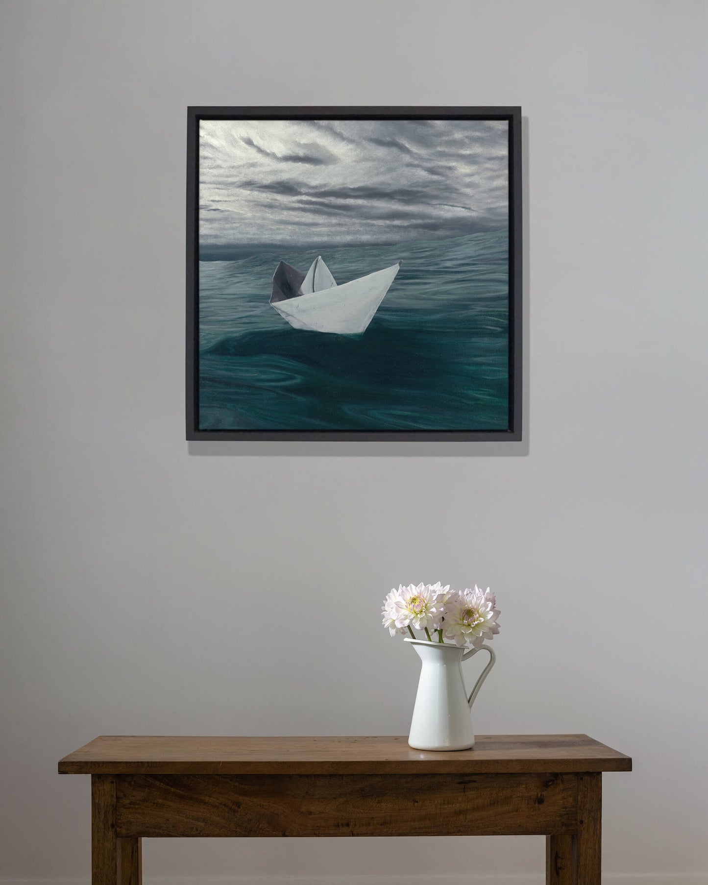 Original art, titled Hope, painted in water mixable oil on canvas, by Australian artist, Hayley Byron. The painting is a depiction of a paper boat, floating in the ocean, with clouds in the background. This image features the artwork in-situ, on a wall in an interior living room.