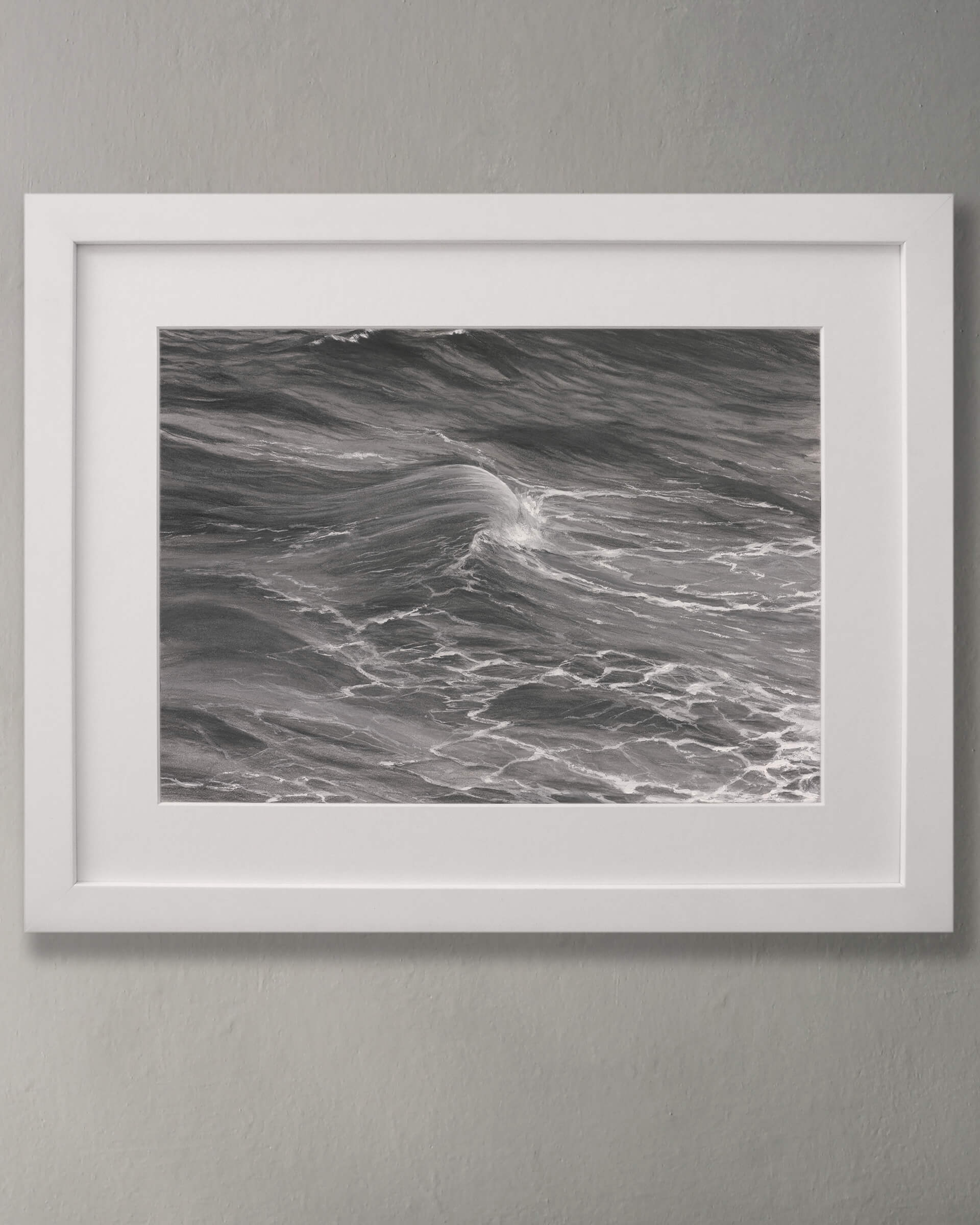 Original art, titled Rise, by Australian artist, Hayley Byron, created with graphite, charcoal, watercolour pencil, and gouache on fine art paper. This drawing is a depiction of the ocean at Tamarama, Sydney, from the viewpoint of the headland cliffs. This image features the artwork in-situ, on a wall in a frame.